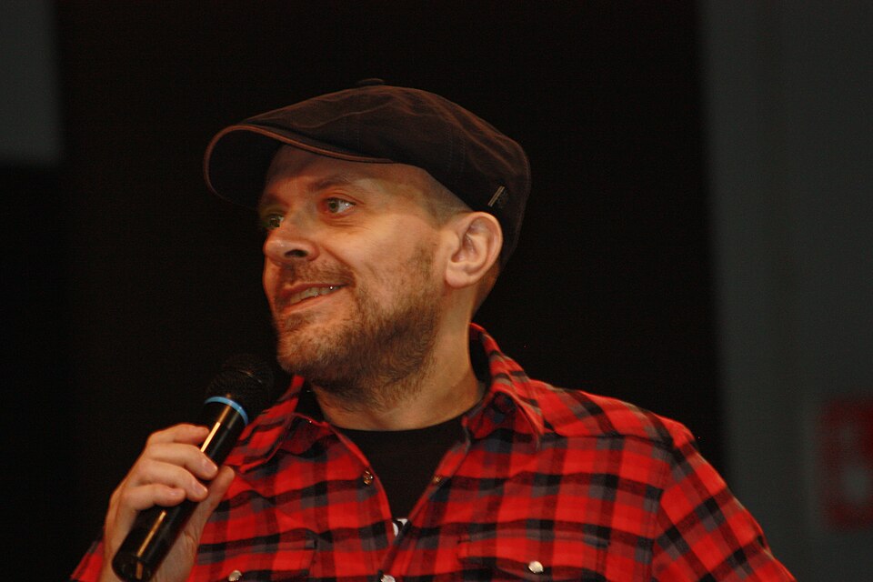 Max Pezzali, cantante degli 883, con cappello scuro, camicia a quadri rossi e microfono a Cartoomics nel 2013
