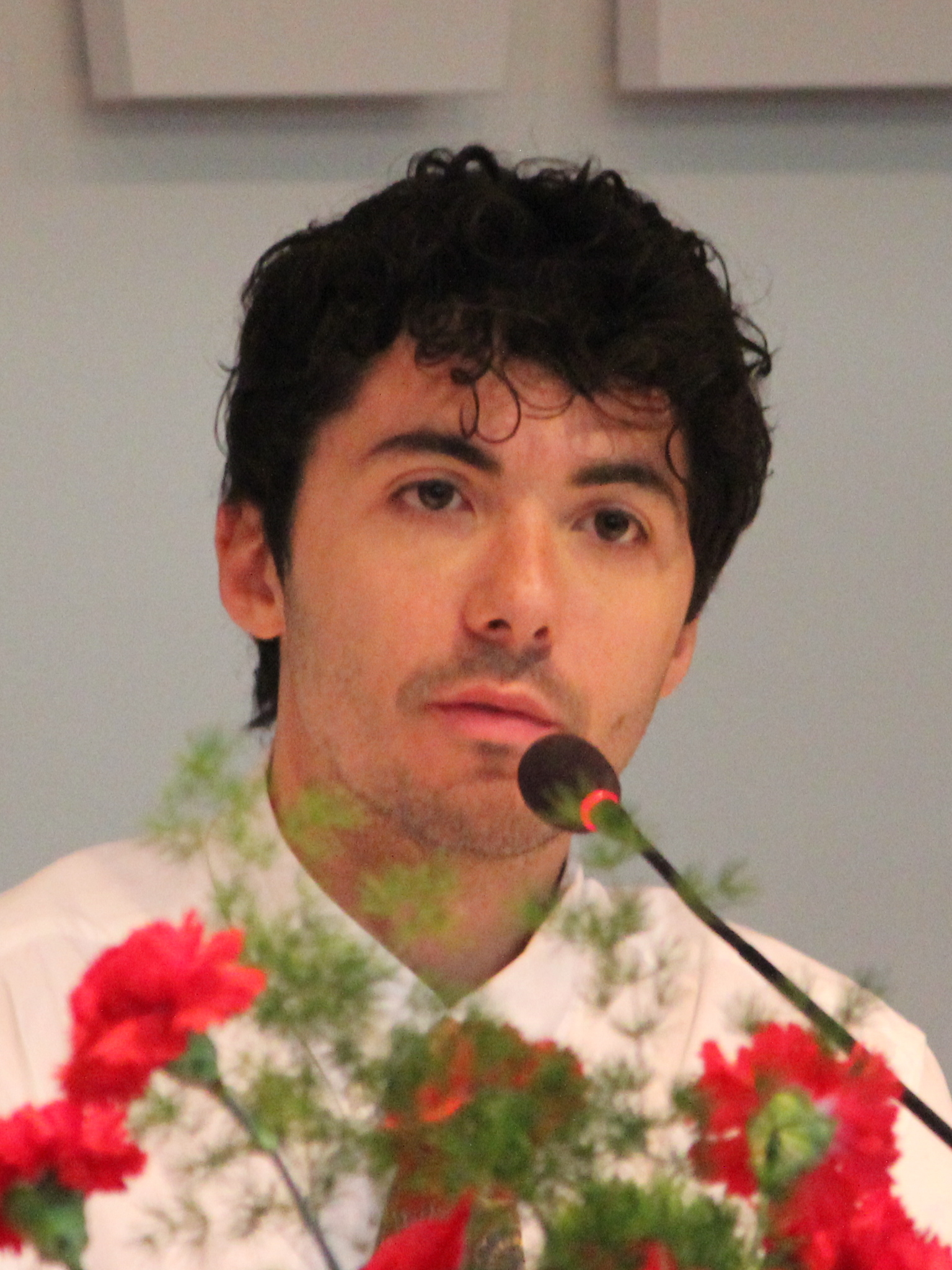 Fulminacci al microfono durante la conferenza stampa del Festival di Sanremo 2026, con fiori in primo piano