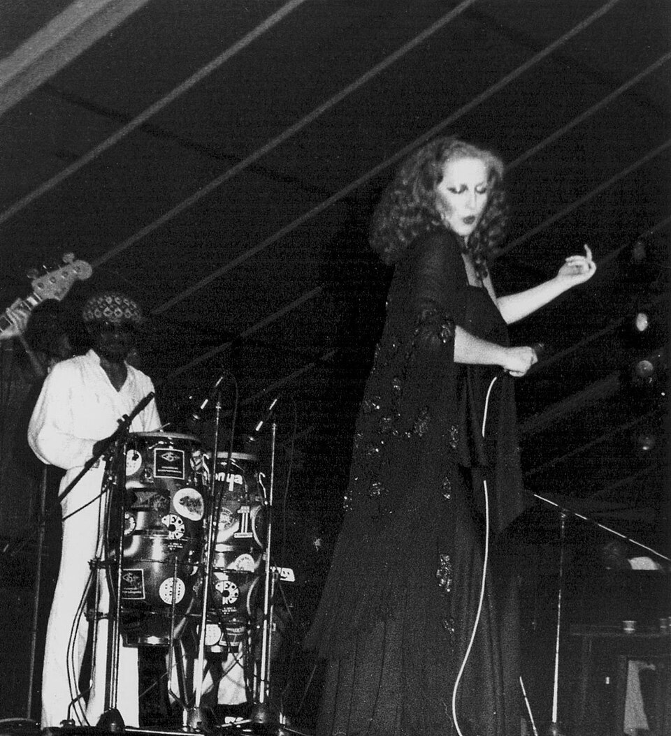 Mina in abito scuro con un microfono, a destra, e il percussionista George Aghedo alle congas, a sinistra, sul palco di Bussoladomani nel 1978; fotografia in bianco e nero