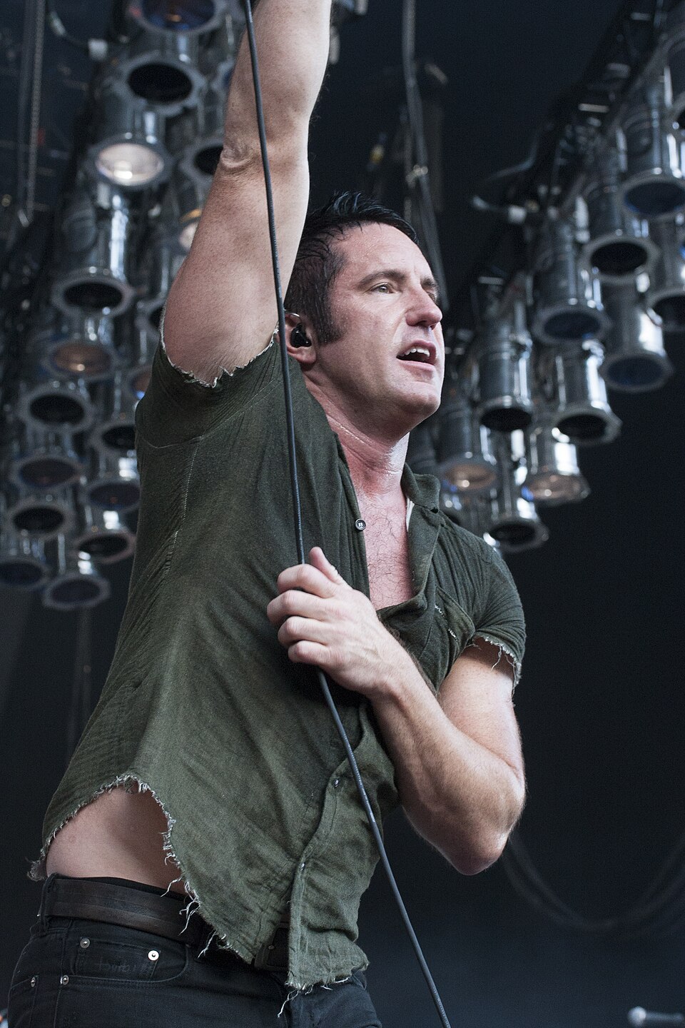 Trent Reznor dei Nine Inch Nails sul palco, con camicia verde e un braccio alzato davanti alle luci; è raffigurato il solo cantante.