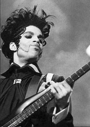 Prince suona una chitarra elettrica sul palco in una fotografia in bianco e nero ripresa dal basso