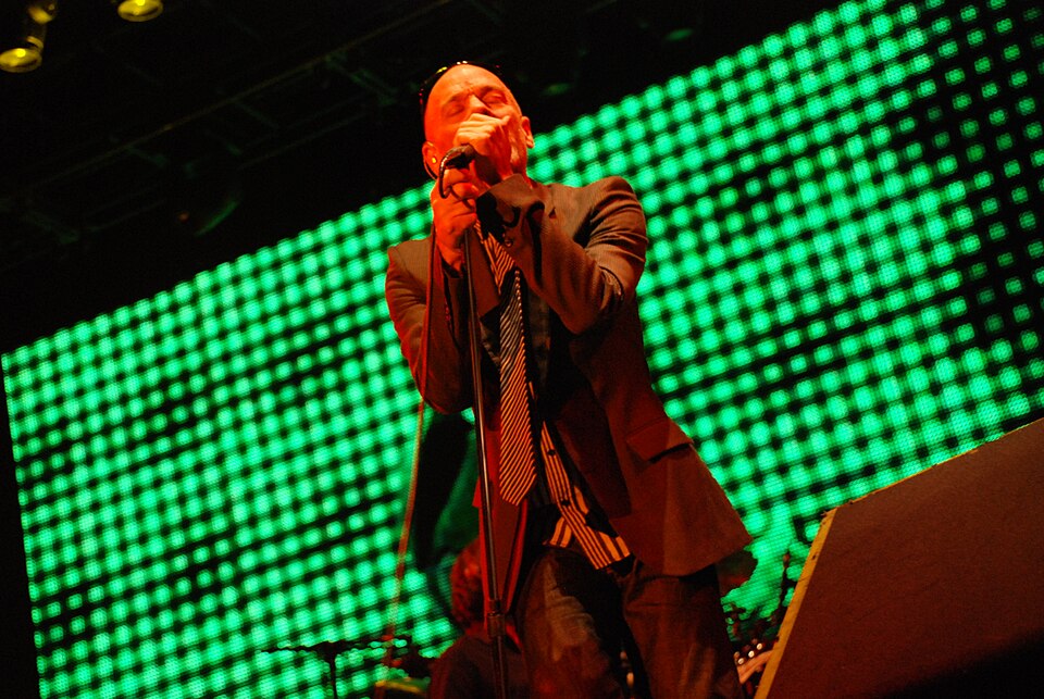 Michael Stipe dei R.E.M. canta al microfono sul palco, davanti a luci verdi