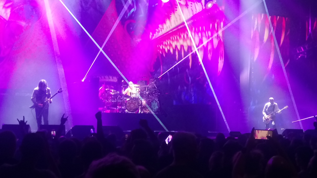 I Tool si esibiscono su un palco illuminato di viola a Birmingham nel 2022, con musicisti e batteria davanti alla scenografia