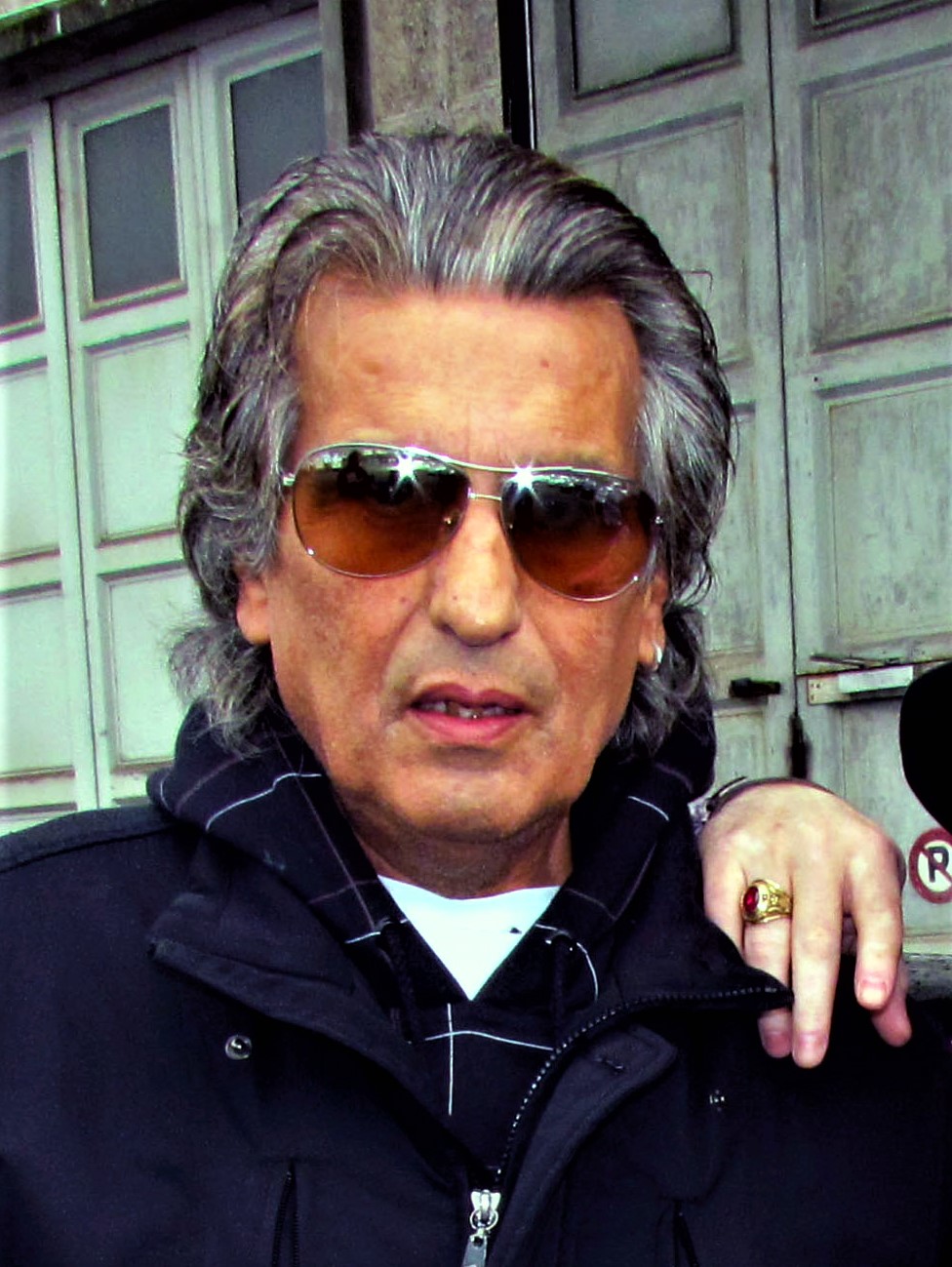 Toto Cutugno con occhiali da sole e giacca scura, fotografato davanti a un portone